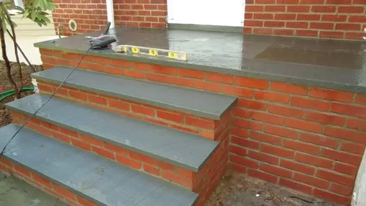 Concrete steps and patio with brick wall and level tool.