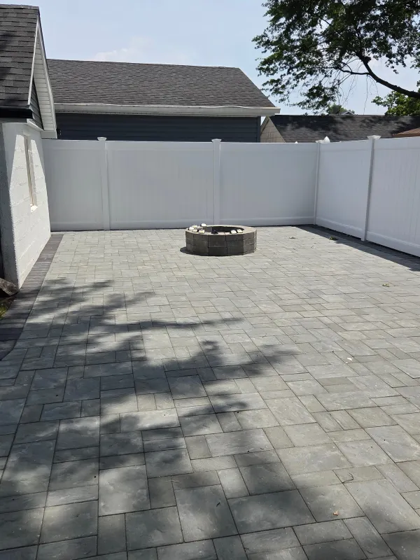 Paved patio with fire pit and white fence.