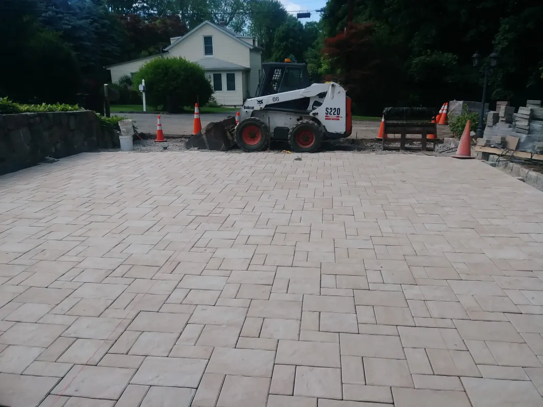 New stone patio under construction with excavator nearby.