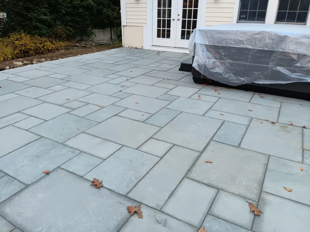 New stone patio with fallen leaves and covered outdoor furniture.