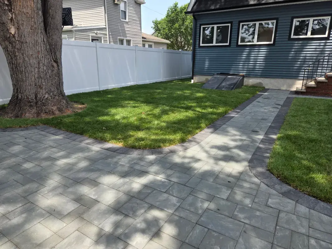 New stone patio and walkway with grass and fence.