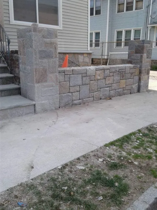 Stone wall and pillars beside concrete steps and sidewalk.